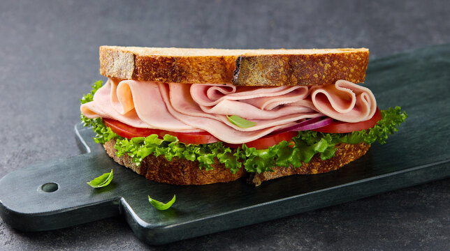 Fresh ham sandwich with tomato lettuce and red onion on toasted artisan bread. Grey background. Close up.