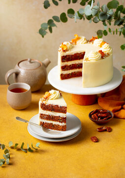 Carrot cake with cream cheese, pecan nuts and mug of tea. Yellow and beige background.