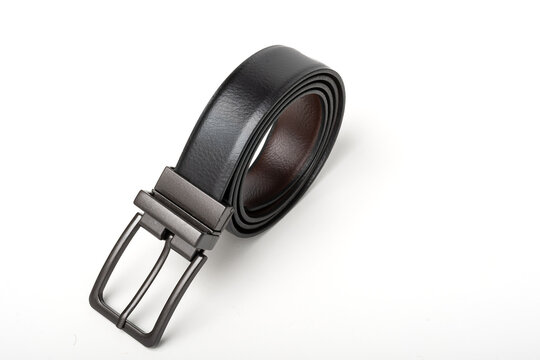 Reversible black and brown men's leather belt with a dark metal buckle, coiled on an isolated white background.