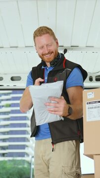 Vertical video of a courier sorts and organizes packages inside a delivery van. Cardboard boxes are stacked around them. It is daytime and the setting shows a busy environment.