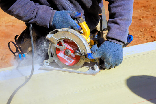 Contractor uses circular saw to cut piece of wood at construction site during build progresses