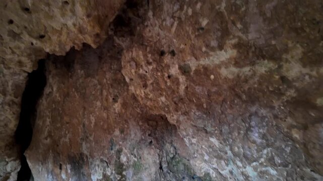 Xemxija, Malta 29.07.2026 - Heritage trail, Roman Baths, shelf like cut in the stone Dark cave walls show rough, textured surfaces. Greenish moss grows on damp, uneven stone. Light filters through nar