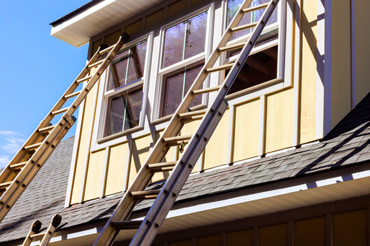 Workers use ladders to reach window on second floor of house during home repair project