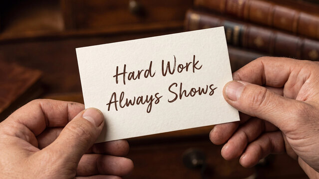 Hands holding a card with the text hard work always shows written on it, against a blurred background of old books
