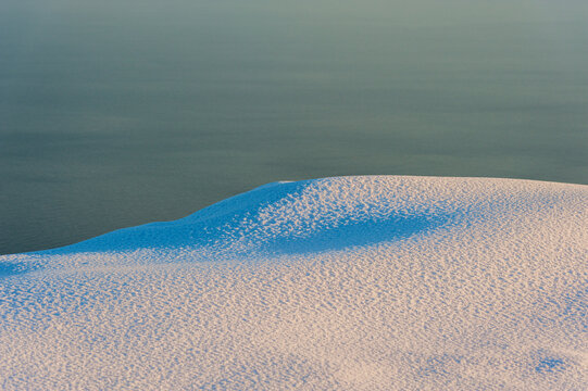 Snowy mountain slope at sunset over sea background.