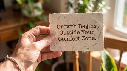 Fototapeta premium Hand holding a piece of handmade paper with the text growth begins outside your comfort zone written on it