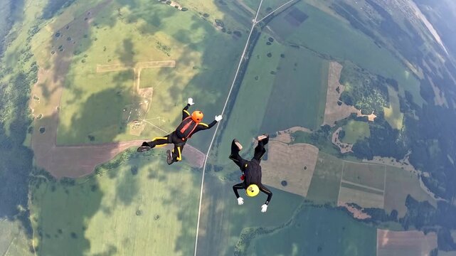 Two athletes perform a group parachute jump in free fall mode over fields and forests. View from a great height.
