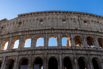 Obraz premium Famous Coliseum in Rome. Colosseum, or Coliseum. Part of the wall of an antique stone structure with arches. Italy, Europe. Famous touristic place in the world, Europe. Beautiful blue sky background.