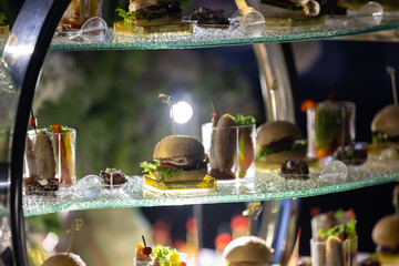 Obraz premium Gourmet Mini Burger Sliders and Appetizers on Glass Display Stand at Luxury Event
