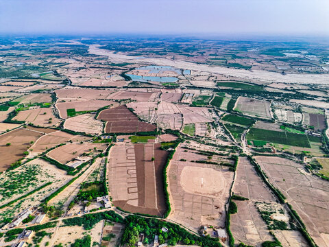 Aerial view of the rural landscape in Wadoor, featuring a patchwork of agricultural fields, irrigation ponds, and scattered trees in the arid terrain of Dera Ghazi Khan, Punjab, Pakistan.