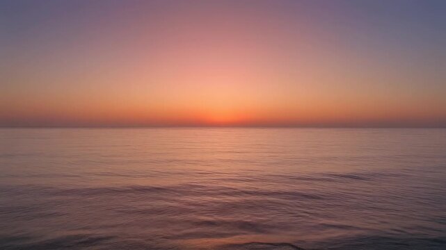 Beautiful serene ocean sunset with soft pink and orange gradient sky over calm tropical water horizon during peaceful evening twilight.