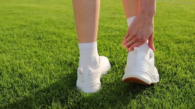Female athlete applies medical adhesive bandage to a heel blister caused by uncomfortable footwear after sports training on a football stadium. Foot care, friction protection, injury prevention