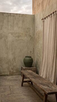 Rustic Minimalist Outdoor Patio with Wooden Bench Clay Jar and Linen Curtain Against Textured Stucco Walls