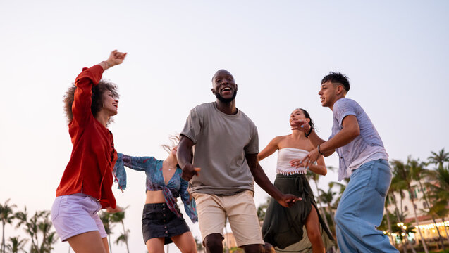Diverse and multicultural friends dancing on the beach during a summer trip, celebrating friendship