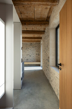 A corridor leading into an empty room with stone walls and a wooden ceiling. A beautiful renovation featuring a polished concrete floor.