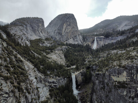 Aerial view of Yosemite Valley featuring cascading waterfalls, rugged granite cliffs, and dense pine forests under a cloudy sky in Yosemite Valley, California, United States.