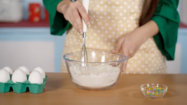 Indian female's hand using a whisker to mix flour and eggs in a bowl - baking concept. Closeup shot of a young home chef's hand whisking a raw egg in maida - the process of making and whisking dough