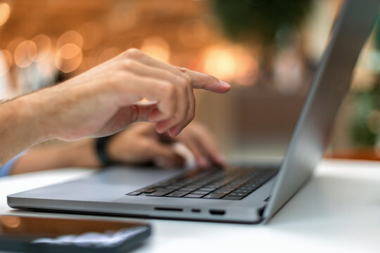 Close-up of a man's hand pointing at a laptop screen while working online against a warm bokeh background. Perfect for business, remote work, technology, and freelance concepts.