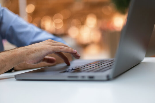 Close-up of a man's hand using a touchpad on a laptop keyboard, working at a white desk with a warm bokeh background. Perfect for freelance, IT, and remote business concepts.