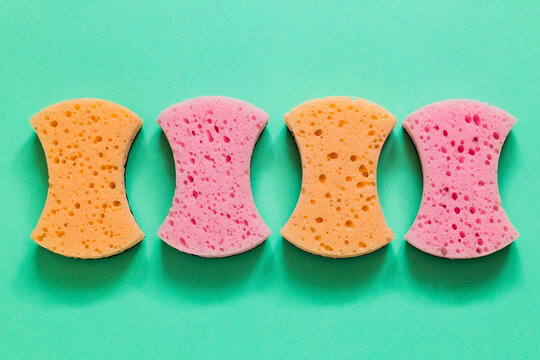 Vibrant kitchen sponges arranged on a solid mint green background, showcasing reusable cleaning supplies in a fresh, minimalist household hygiene composition.
