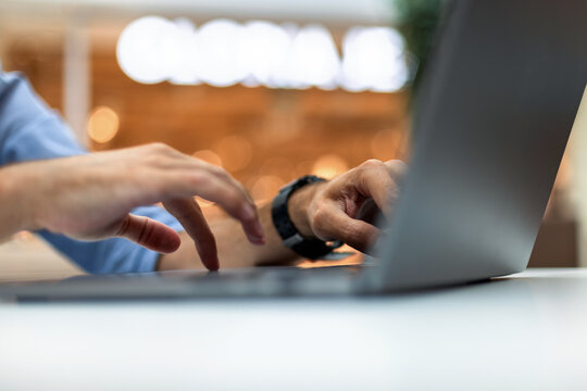Close-up of a businessman's hands typing on a laptop keyboard at a desk, with a bright bokeh background. Perfect for concepts of remote work, freelance, programming, and digital technology.