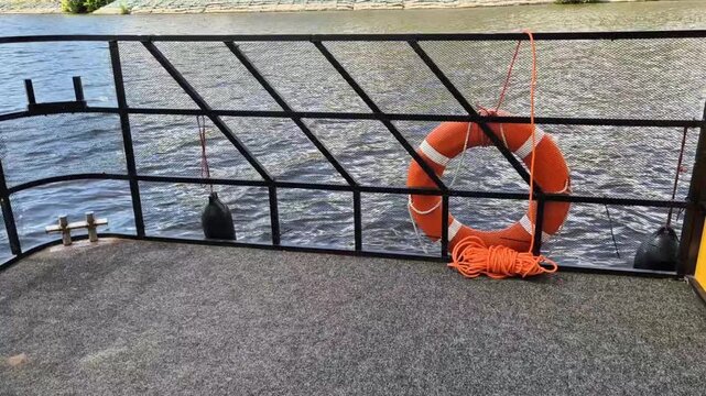 Orange lifebuoy on moving riverboat deck railing with flowing water texture in daylight. Concept: vessel passenger security