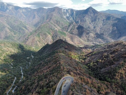 Aerial view of Sequoia National Park featuring a winding mountain road with sharp switchbacks surrounded by rugged forested slopes and high peaks in Tulare County, California, United States.