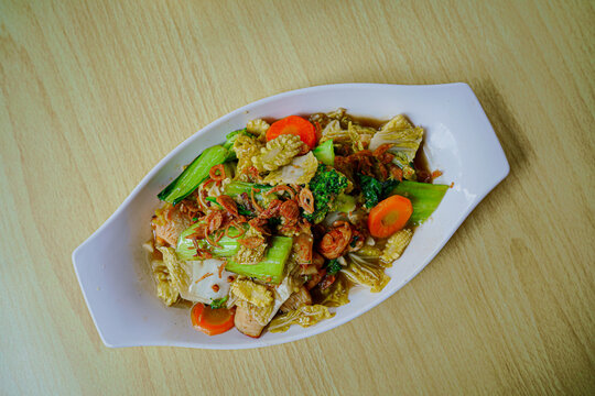 A delicious plate of homemade Indonesian capcay, featuring stir-fried fresh vegetables like carrots, broccoli, and cabbage served warm on a wooden table, perfect for healthy food concepts.