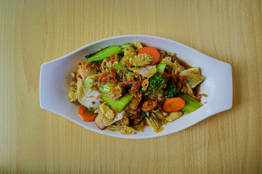 A delicious plate of homemade Indonesian capcay, featuring stir-fried fresh vegetables like carrots, broccoli, and cabbage served warm on a wooden table, perfect for healthy food concepts.