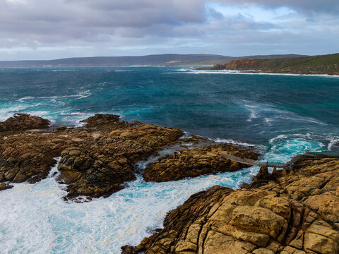 Aerial view of Canal Rocks Bridge with rugged granite rock formations, crashing turquoise ocean waves, and dramatic cloudy sky in Yallingup, Western Australia, Australia.