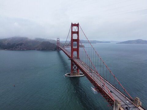 Aerial view of the Golden Gate Bridge spanning the bay with traffic on the deck, surrounded by misty hills and deep blue water in San Francisco, California, United States.