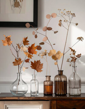 Clear glass smoky bottles vases set various dried botanical branches maple leaves eucalyptus stems interior rustic aesthetic seasonal decor tabletop arrangement