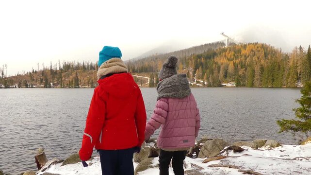 Two little beautiful girls walk along shore of winter lake of Strbske Pleso, is favorite ski, tourist, and health resort in High Tatras, Slovakia.