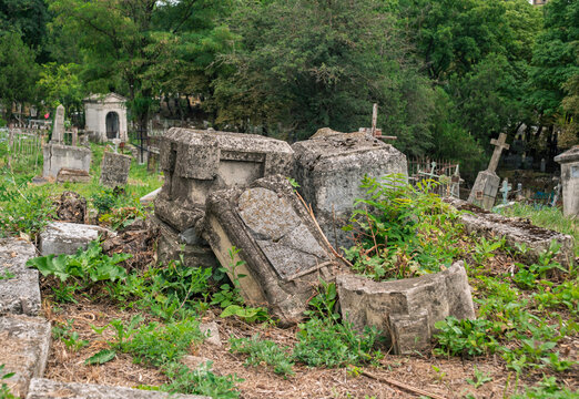 Crumbling stone monuments scattered across ancient overgrown cemetery during daylight hours