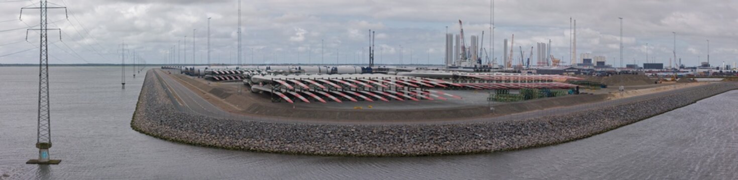 Aerial view of Esbjerg harbour with rows of wind turbine blades and tower components stored for transport, power lines, and the North Sea in Esbjerg, Syddanmark, Denmark.