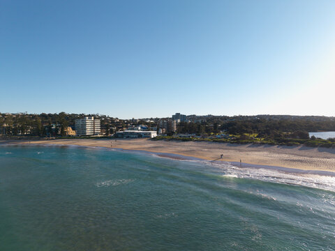 Aerial view of Dee Why beach with golden sand, turquoise waves, and coastal buildings in Dee Why, New South Wales, Australia.