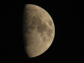 Detailed telephoto shot of first quarter moon surface with visible craters against dark space © Elisa