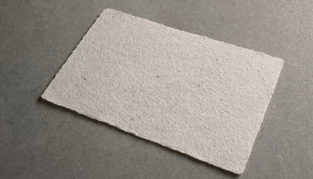 A single rectangular sheet of off-white handmade paper with a rough deckle edge placed on a flat, neutral grey surface for a minimalist display