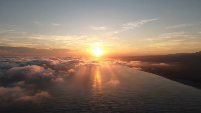 Sunrise over ocean with clouds reflecting golden light, showcasing the gradual illumination of the horizon and the serene coastal landscape at dawn
