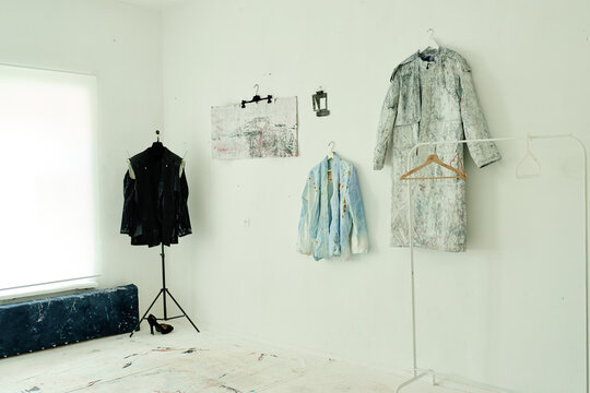 Wide shot of contemporary artist studio displaying painted garments on hangers and mannequin, presenting wearable art collection. For fashion branding, gallery promotion, creative industry marketing