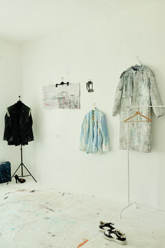 Vertical image of contemporary artist studio displaying painted garments and footwear, presenting wearable art collection. Suitable for fashion branding, gallery promotion, creative editorial