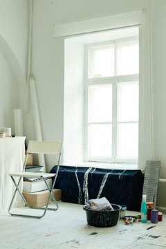 Vertical image of contemporary artist studio showing chair, paint buckets, brushes, canvas materials near window. Supporting creative business branding, art workshop promotion, vertical