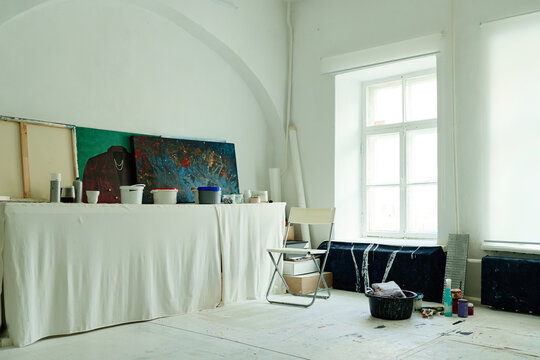 Wide shot of contemporary artist studio displaying canvases, paint containers, chair, creative workspace for producing modern artwork. For art education, gallery promotion, creative industry marketing