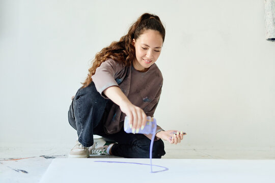 Young adult Caucasian woman pouring paint onto canvas while creating contemporary artwork in studio, expressing creativity, artistic process. For artist branding, gallery promotion, creative workshops