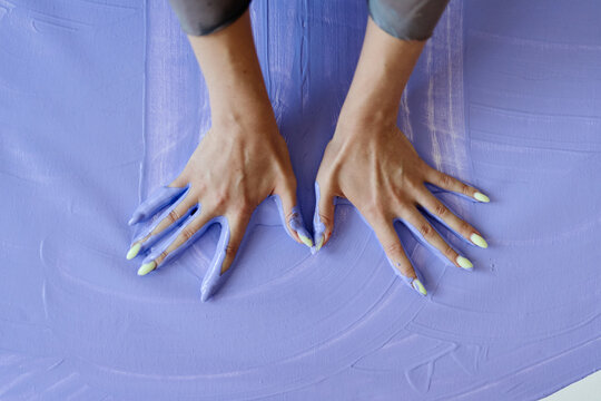 Close up of young adult woman hands pressing into lavender paint, showcasing contemporary body art and creative experimentation. Ideal for artist branding, gallery promotion, workshop ads