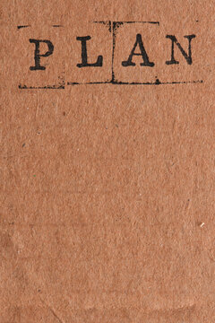 Stamped word PLAN on top brown craft paper background featuring generous lower copy space.