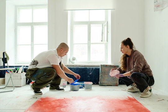 Wide shot of young adult artists mixing paint and preparing canvas in studio, creating contemporary artwork. Ideal for creative industry marketing, art education, gallery promotion