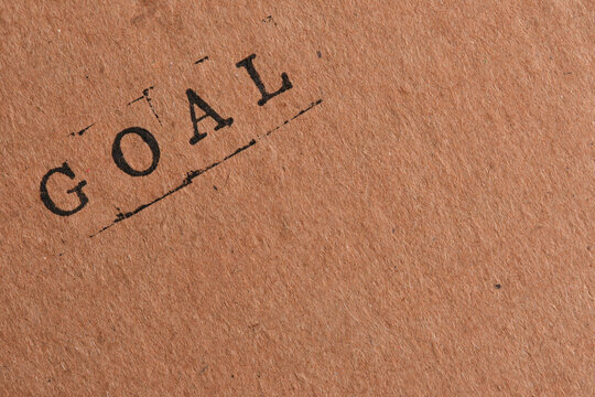 Diagonal typography word GOAL stamped on brown craft paper with large negative space area.