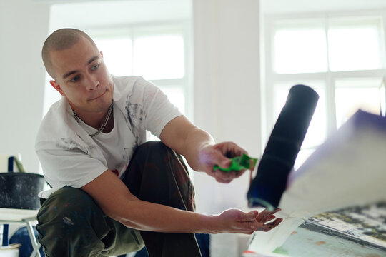 Young adult Caucasian man creating artwork with paint roller in studio, expressing contemporary artistic process. Useful for creative industry marketing, artist branding