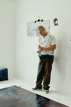 Vertical shot of young adult Caucasian male artist mixing paint in studio, preparing contemporary artwork and creative process content. Ideal for art education, culture marketing